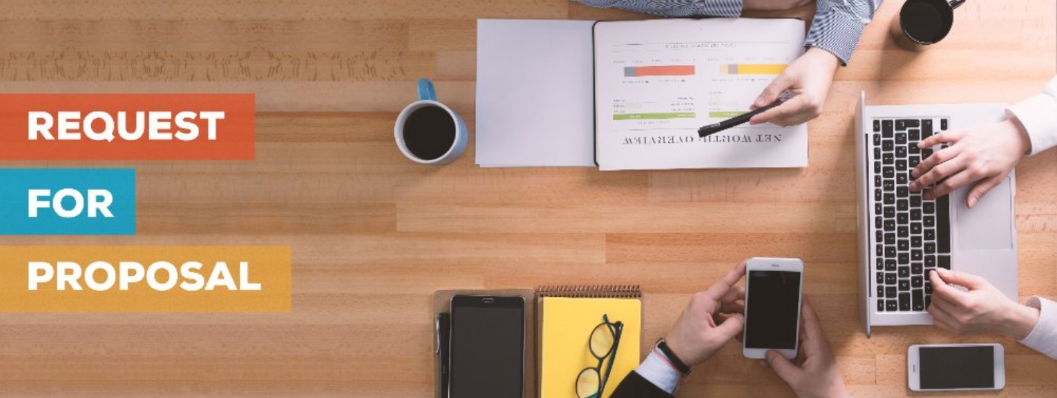 Team working on a Request for Proposal (RFP) with laptops, documents, and phones on a wooden desk.